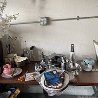 Photo of various kitchen appliances and tools on a wooden table including French press, manual juicer, grater, digital scale, ceramic egg cups, mixing bowls, scissors, and metal utensils.