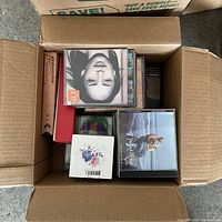 Top-down view of open box showing a mix of CD jewel cases with various cover artworks from different artists and genres.
