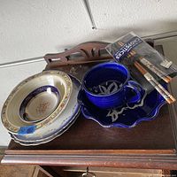 Photo showing a deep blue ceramic mug with a scalloped matching saucer, three decorative ceramic dishes in varied floral patterns, and a sealed pack of chopsticks with three pairs.