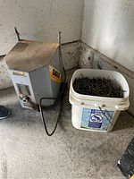 Photo of Eagle metal device next to bucket of nails on the floor.
