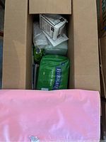 Top-down photo of open cardboard box with visible medical supplies inside including FitRight adult briefs in green packaging, a small white box likely containing masks or similar items, and other plastic wrapped medical supplies.