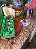 Overall view of wooden bowls, plates, ceramic eggs, serving utensils, wooden cutting board, and metal container with pink mat.