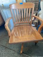 Front view of a wooden swivel office chair showing slatted backrest, curved armrests, and caster wheels on base.