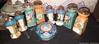 Full set of 9 hand-painted Nippon style salt and pepper shakers and a covered bowl, showing varied pastel colors with detailed floral artwork and metal tops on shakers.