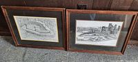Both framed prints side by side showing wooden frames and glass fronts containing cityscape line drawing prints.