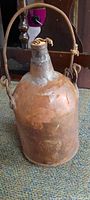 Full view of the 8 inch antique jug showing metal handle and top cloth wrapping.