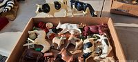 Overview of several antique plastic farm animals including cows, horses, pigs, and accessories like pitchfork and red wagon inside a cardboard box.