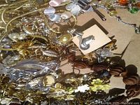Photo showing an assortment of vintage jewelry including pearl necklaces, metal pins with various designs, and other metallic costume jewelry.