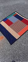 Full view of the handmade patchwork quilt laid flat on pavement, showing the colorful fabric patches and sewn border.