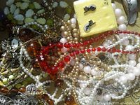 Photo showing strands of necklaces with red beads, faux pearls, amber beads, and yellow stud earrings inside a yellow box