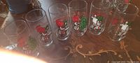 Six vintage Holly Hobby glasses with Christmas character and tree designs arranged in a row on a wooden surface.