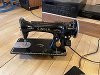 Full side view of the black antique Singer sewing machine showing gold floral detailing and hand crank.