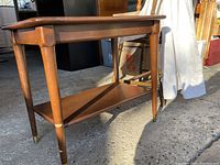 Side angle view showing side table's tapered legs with brass caps and lower shelf