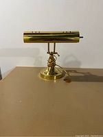Brass piano lamp on a flat surface showing the full lamp profile with adjustable shade and attached power cord.