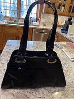 Black leather purse with gold trim displayed upright on a kitchen counter, showing front exterior and shoulder straps.