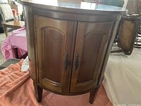 Round wooden liquor cabinet with double front doors and metal handles shown from the front on a cloth surface.