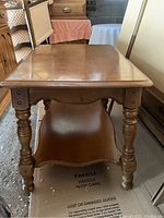 Front view of solid wood side table showing rectangular top, carved legs, and curved lower shelf.
