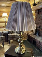 Close up photo of lamp's pleated beige fabric shade and brass base in a log cabin style living room