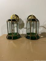 Front view of two gold-colored wall sconces with green cut glass panels showing overall design and details.