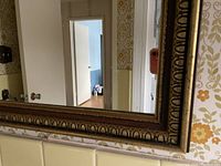 Close-up of vintage mirror frame mounted on wall with floral wallpaper background