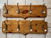 Two wooden hanging racks laid flat, each with four brass hooks with white ceramic ends visible