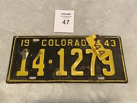 Front view of 1943 Colorado license plate with attached 1944 validation tab, showing plate number 14-1279 and condition details including scratches and rust.