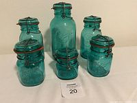 Photo showing the full set of six blue tint Ball jars with metal bale lids and orange rubber gaskets on a white cloth background.