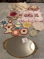 Overview of assorted vintage crochet potholders with an oval mirrored tray in front