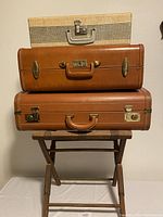Stacked view of three vintage suitcases in beige and brown colors showing exterior condition and hardware details