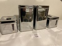 Four Lincoln BeautyWare metal canisters with lids arranged side by side, from left to right labeled Coffee, Flour, Sugar, and Tea, showing front views with labels.