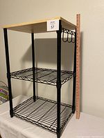 Photo shows one black metal wire shelving unit, three wire shelves, light wood top, side metal hooks visible, height approximately 32.5 inches, width 20 inches.
