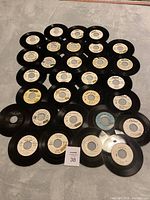 Overview photo showing 33 black vinyl 45 RPM records spread out on a surface with various label colors and the lot number card visible.