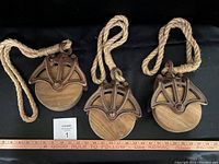Set of three reproduction pulleys laid out with rope attached, showing wooden wheel and rusted metal frame.