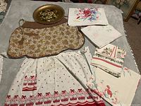 Full view of three vintage aprons, assorted folded table linens, and the hand-painted Nashco tray on table surface.
