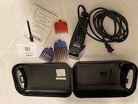 Wahl clipper with power cord, four colored guide comb attachments (two purple, one red, one blue), and black plastic carrying case inside with lid open.