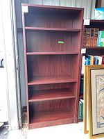 Front view of tall bookshelf with five shelves, reddish mahogany wood tone, and some scratches visible on the shelves.