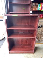 Full front view of the wooden bookshelf with four shelves and dark wood finish, showing overall condition and surface wear.