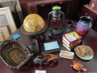 Wide shot of assorted vintage decorative items on dark wood table, showing globe, lantern, basket, ceramic vase, wood figures, coin bank, decorative plates, and books.