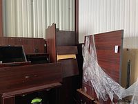 Disassembled dark wood office desk parts stacked together showing drawers, table tops, and panels.