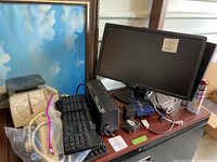 Full shot of the electronics lot showing Dell monitor, keyboards, postal scale, surge protector, Netgear router, and cables on a wooden surface.