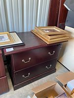 Full view of wood filing cabinet showing two drawers with metal handles and picture frames stacked on top.