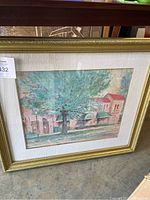 Front view of framed signed painting showing central large green tree and buildings with red roofs under textured glass and gold frame.