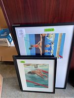 Two framed photos leaning against a wood background, showing aquatic Olympic sports athletes. Visible auction sticker 431 on smaller frame.