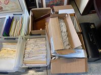 Overview of several plastic bins containing labeled folders and dividers, with cardboard boxes on top containing more office supplies