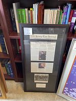 Framed article featuring a New Jersey Law Journal article and signed memorabilia with some dust and smudges.