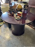 Round wooden table with various items on top including an old globe, books, and decorative objects, located in a storage or warehouse space.