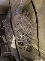 Pile of clear acrylic display stand parts in a plastic bag, showing multiple pieces that need assembly to form stands.