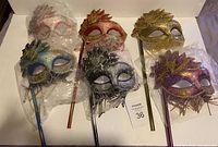 13 handheld masquerade masks in varied color schemes with sticks, grouped and plastic wrapped in some cases