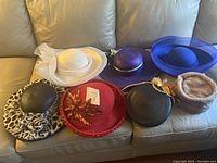 Seven ladies fashion hats displayed on a couch showing variety in style including wide-brimmed, fur, and embellished hats.