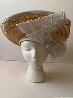 Front view of natural straw Mr John Moderne hat with large white decorative bow